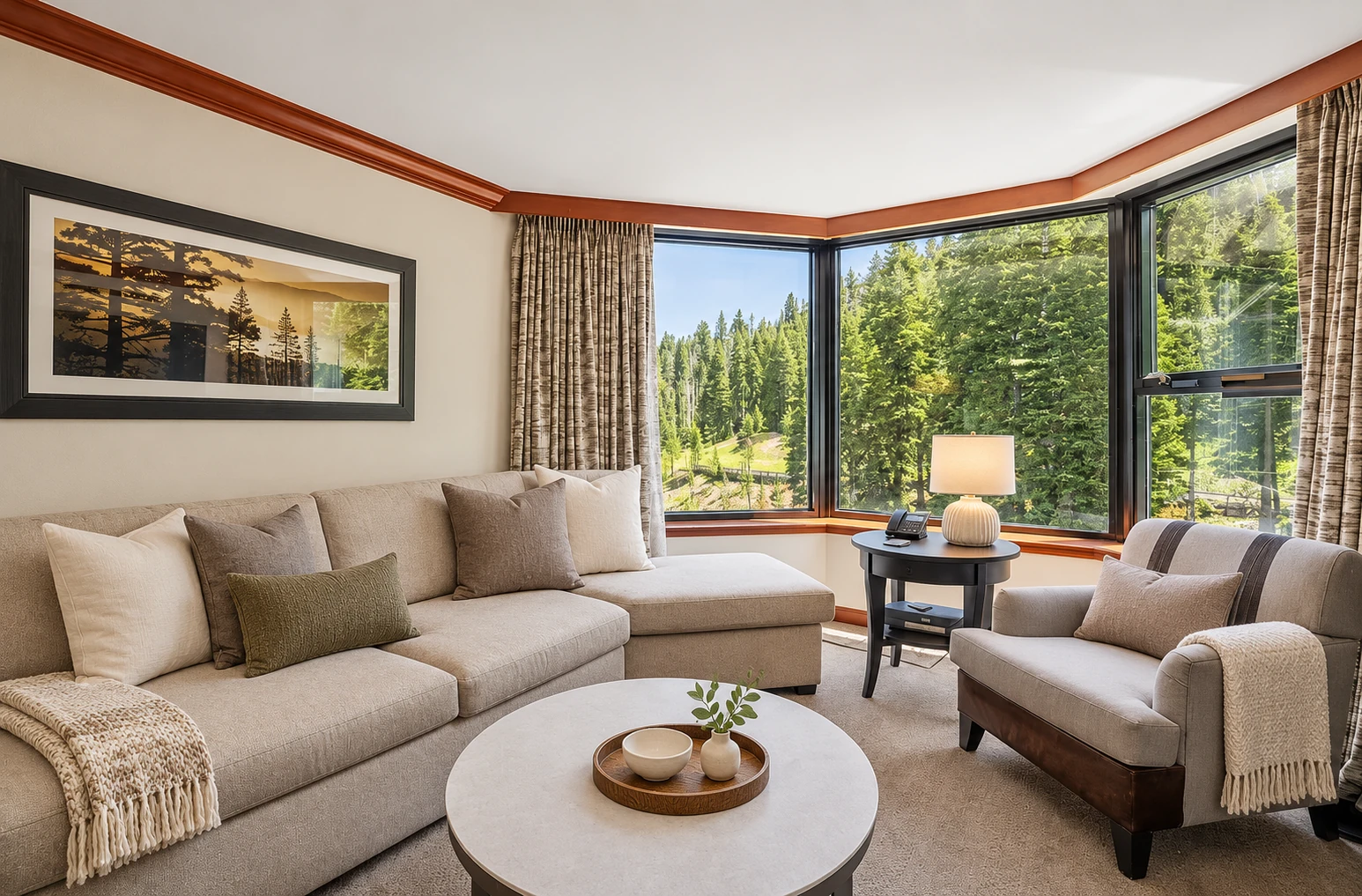 One- and two-bedroom suites — Private corner living area with sofa, seating, and forest-facing windows; digitally styled linens and accessories